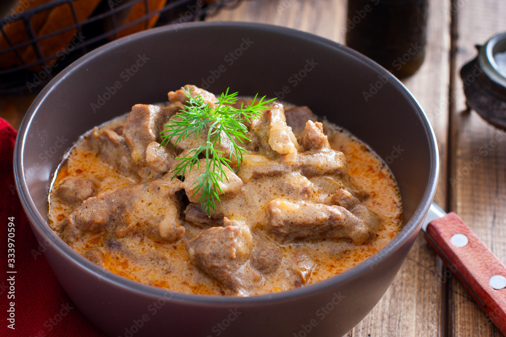 Traditional beef stroganoff in a ceramic bowl on a wooden table, selective focus Traditional beef stroganoff in a ceramic bowl on a wooden table, selective focus