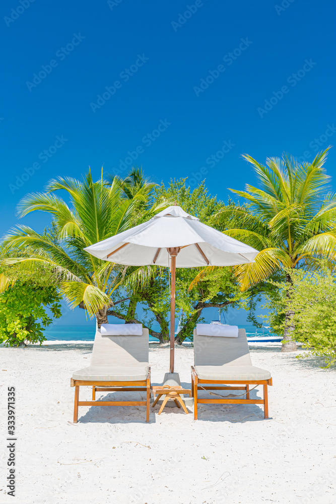 Tropical island beach, loungers or beach beds with umbrella with palm trees background. Luxury summer travel or holiday concept