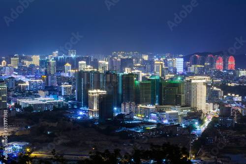 Night view of Sanya city with bright multi-colored illumination buildings, structures, roads, sidewalks, poles, bridges.