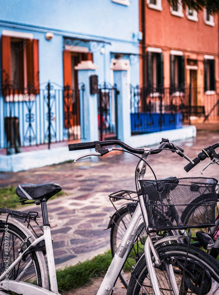 bicycles parked in the foreground on a street in Italy, against an unfocused background of colored houses.