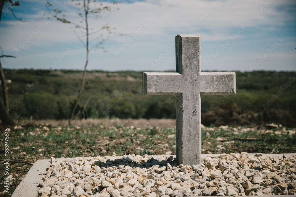 Single concrete cross shaped headstone grave marker stands at the top of a hill overlooking the horizon to commemorate a life