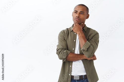 Portrait of thoughtful african-american man taking decision, look focused and serious, touch chin gazing upper left corner as if making choice, picking product, pondering over white background