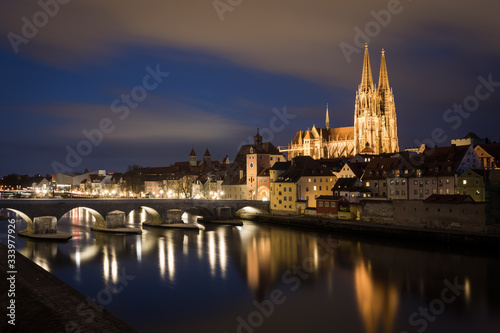 Illuminated saint Peter cathedral with historical stone bridge after dark in Regensburg, Bavaria, Germany. Cityscape image over the Danube river from Sorat Hotel terrace.