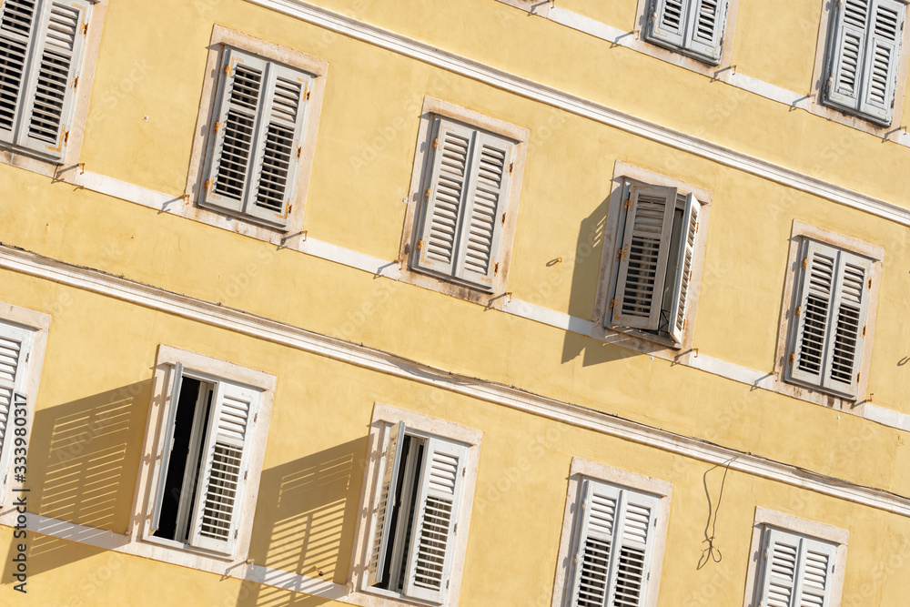 Fototapeta premium Traditional Mediterranean style building with white shutters on yellow wall