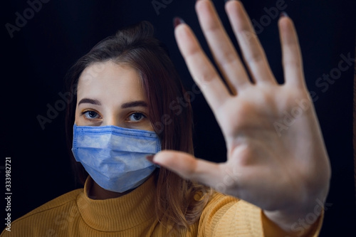 Young woman in blue medical mask on black background. Coronavirus protection