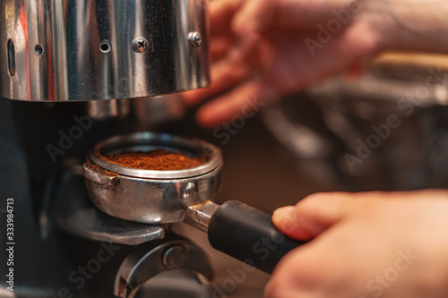 A Barista grinds coffee beans into a holder on a coffee grinder.