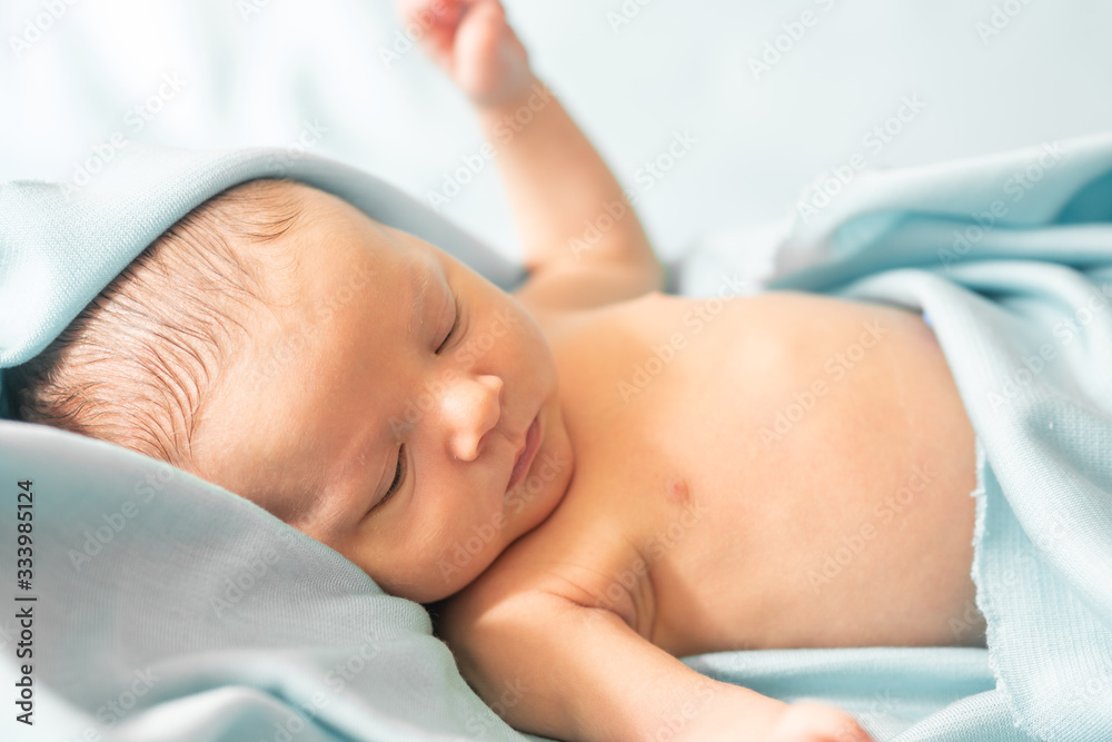 naked newborn baby covered with fluffy blue towel after his first relaxing bath. New born baby hygiene, baby care concept.
