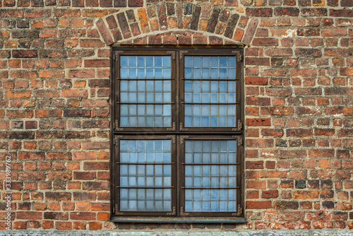 Antique Old wooden window with metal fittings and hinges in old red brick wall of an ancient European castle.