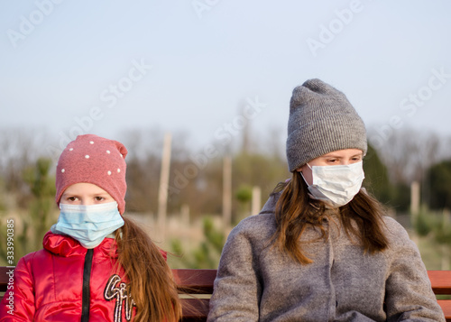 Mom with daughter in medical masks in a park on a bench. Coronavirus protective mask. Covid-19. Young woman with a child in medical masks