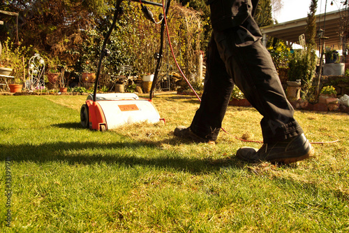 Aeration with a scarifier. Lawn thatcher in action. Using a scarifier in the garden to improving quality of the lawn in spring. a worker man, Gardener Operating Soil Aeration Machine on Grass Lawn.  photo