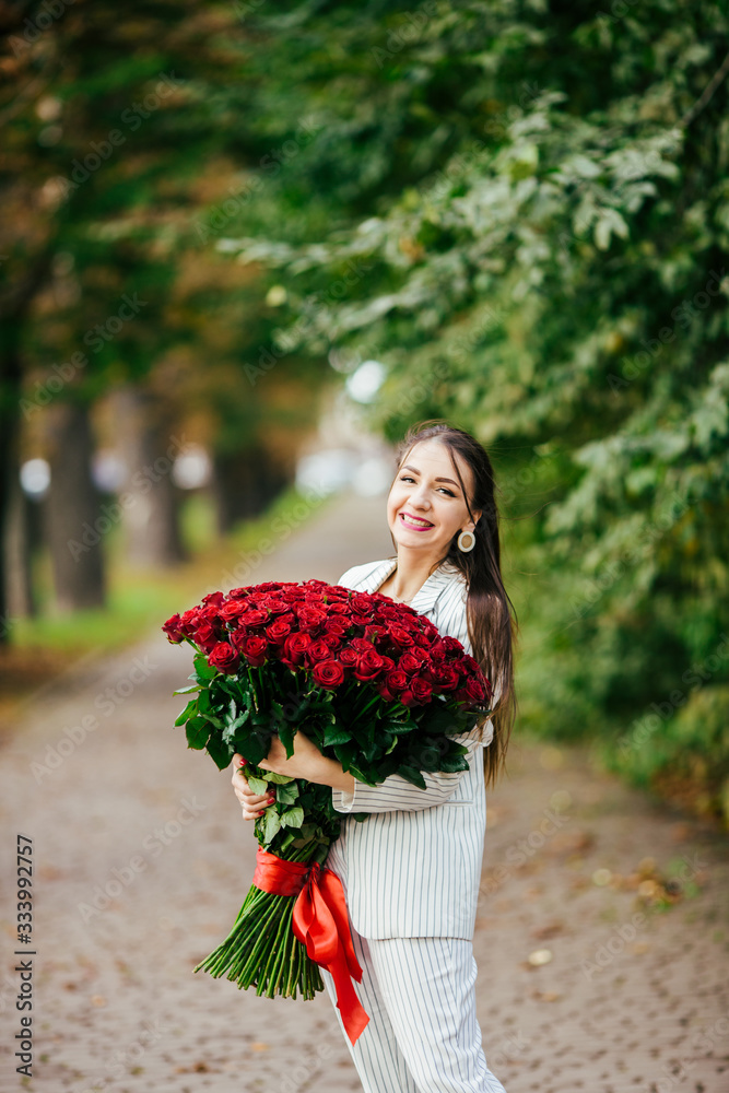 Fototapeta premium Beautiful girl in a suit with flowers in the hands of a rose on a green background