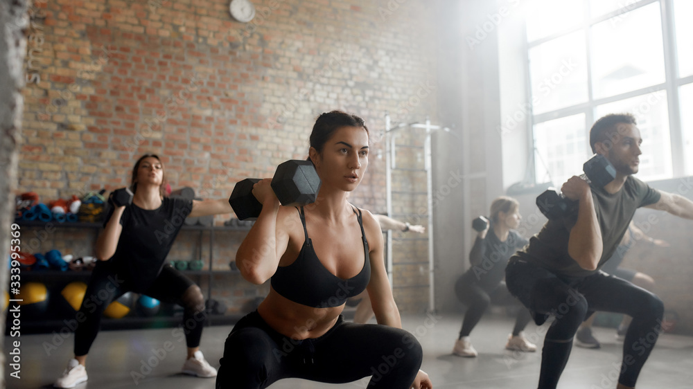 Play strong. Young athletic woman lifting dumbbell while having workout at industrial gym. Group training concept Play strong. Young athletic woman lifting dumbbell while having workout at industrial gym. Group training concept