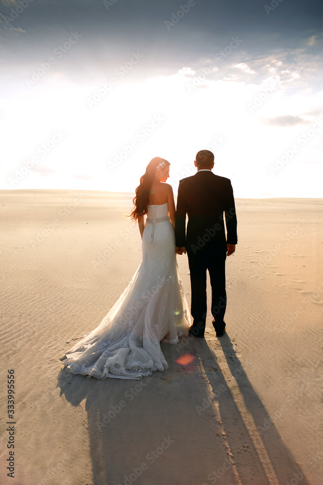 Bride and groom holding hands in the sand desert at sunset Bride and groom holding hands in the sand desert at sunset