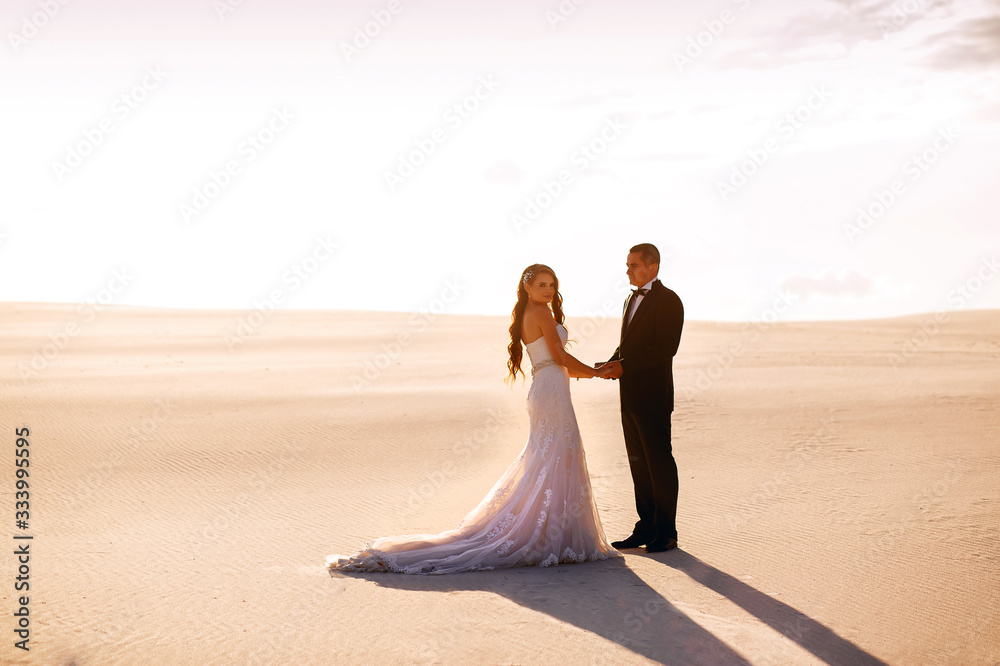 Bride and groom holding hands in the sand desert at sunset Bride and groom holding hands in the sand desert at sunset