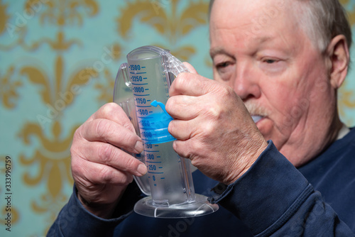 Elderly man using incentive spirometer for breath improvement.  Helpful for pneumonia or a lung condition like chronic obstructive pulmonary disease (COPD) or cystic fibrosis. 