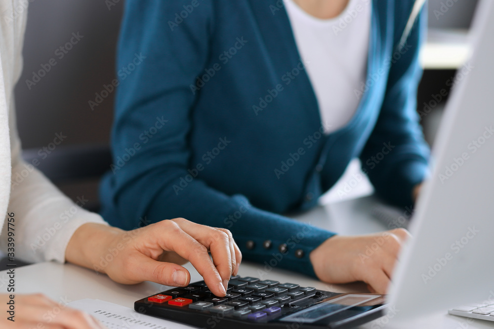 Accountant checking financial statement or counting by calculator income for tax form, hands closeup. Business woman sitting and working with colleague at the desk in office. Tax and Audit concept Accountant checking financial statement or counting by calculator income for tax form, hands closeup. Business woman sitting and working with colleague at the desk in office. Tax and Audit concept