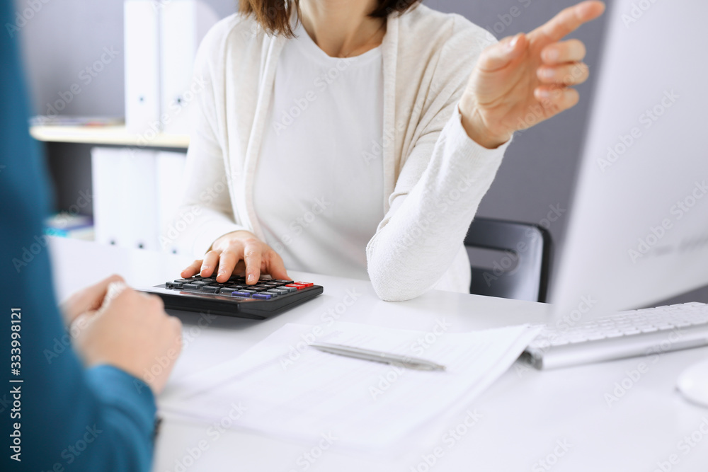 Accountant checking financial statement or counting by calculator income for tax form, hands closeup. Business woman sitting and working with colleague at the desk in office. Tax and Audit concept Accountant checking financial statement or counting by calculator income for tax form, hands closeup. Business woman sitting and working with colleague at the desk in office. Tax and Audit concept