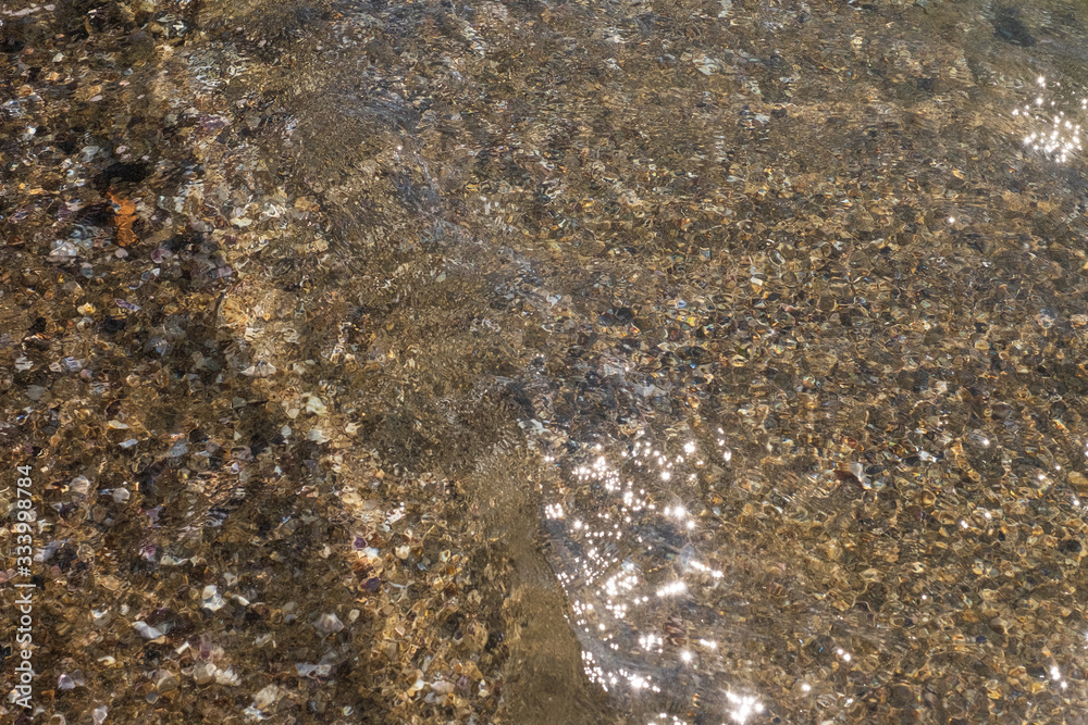 Water on the beach. Waves, stones and sand. The sun glare from the water on the sand. 