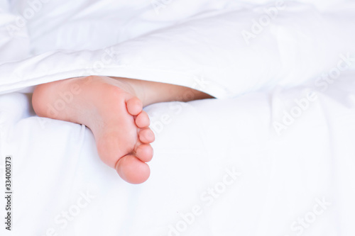 Child feet under the clear soft white blanket. Tenderness of morning dream