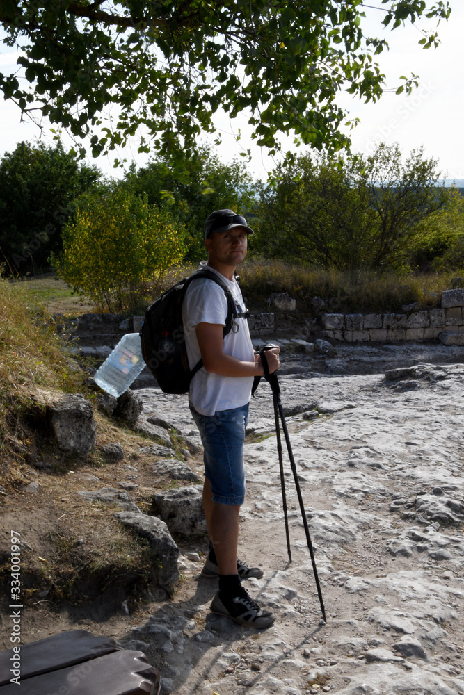 A young man in shorts and with Scandinavian sticks walks around the picturesque places, and behind his back is a backpack and a bottle of water.