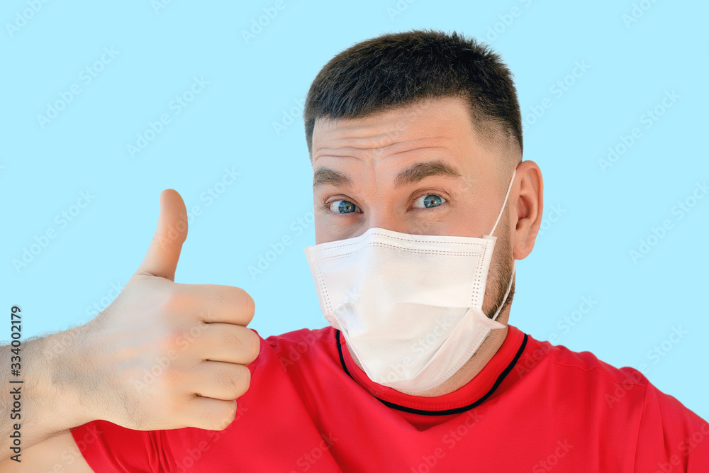 young man in a medical mask with a positive cheerful look and a thumbs up protects himself from viruses young man in a medical mask with a positive cheerful look and a thumbs up protects himself from viruses