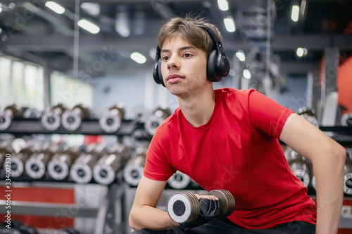 young man in sports clothes and headphones works out with dumbbells in the gym