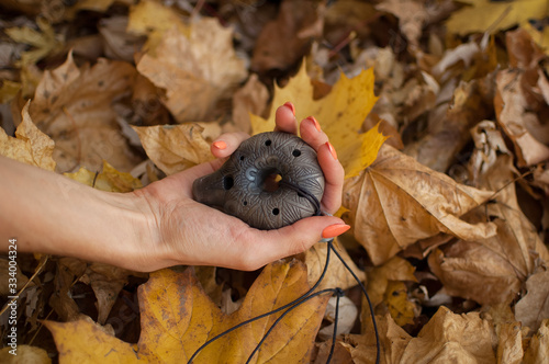 Female hand with orange manicure holds ceramic ocarina in the forest during autumn. Relaxing tranquil scene, traditional music concepts photo