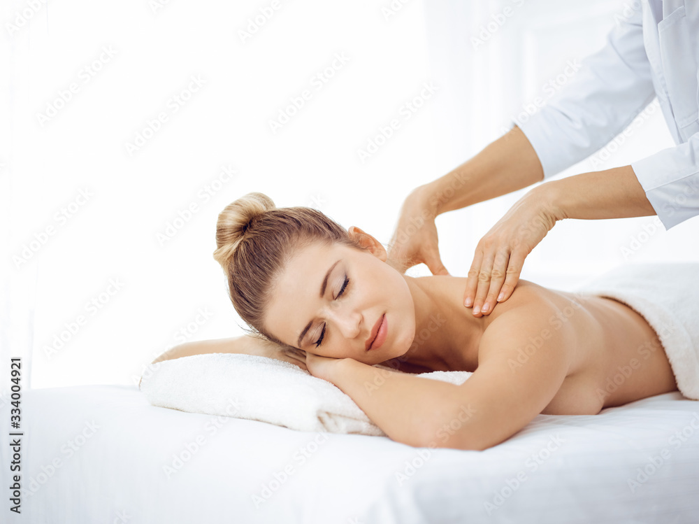 Young and blonde woman enjoying massage of back in spa salon. Beauty concept Young and blonde woman enjoying massage of back in spa salon. Beauty concept