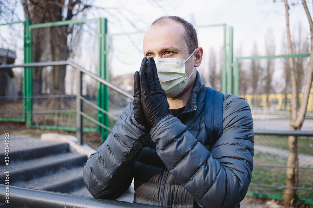 Sad man in yellow surgical mask and black gloves is praying on the street. Pandemic coronavirus 2020. Quarantine.Virus concept. Epidemic infection. Sad man in yellow surgical mask and black gloves is praying on the street. Pandemic coronavirus 2020. Quarantine.Virus concept. Epidemic infection.