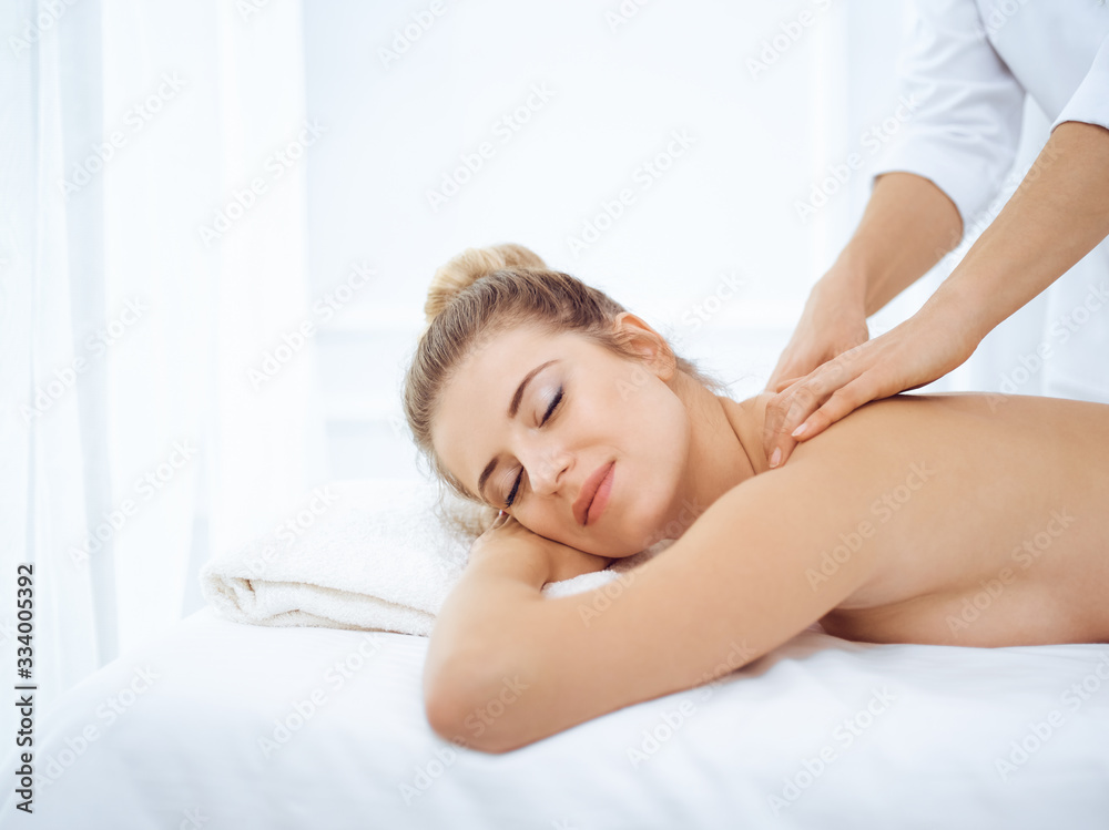 Young and blonde woman enjoying massage of back in spa salon. Beauty concept