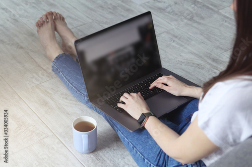 Girl works from home behind a laptop, girl sits on the floor of the house and works