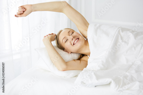 Smiling woman stretching hands in bed after waking up, entering a day happy and relaxed after good night sleep. Sweet dreams, fairy morning concept