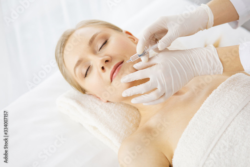 Beautician doctor doing beauty procedure with syringe to caucasian female face. Cosmetic medicine and surgery, beauty injections concept