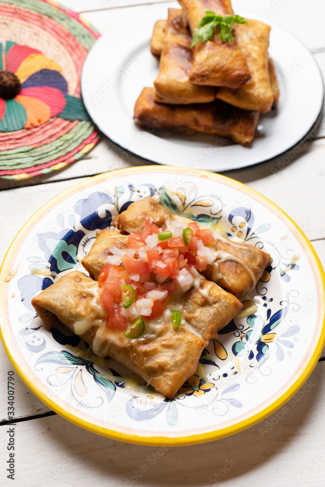 Mexican chimichanga with melted cheese and pico de gallo sauce on white background Mexican chimichanga with melted cheese and pico de gallo sauce on white background