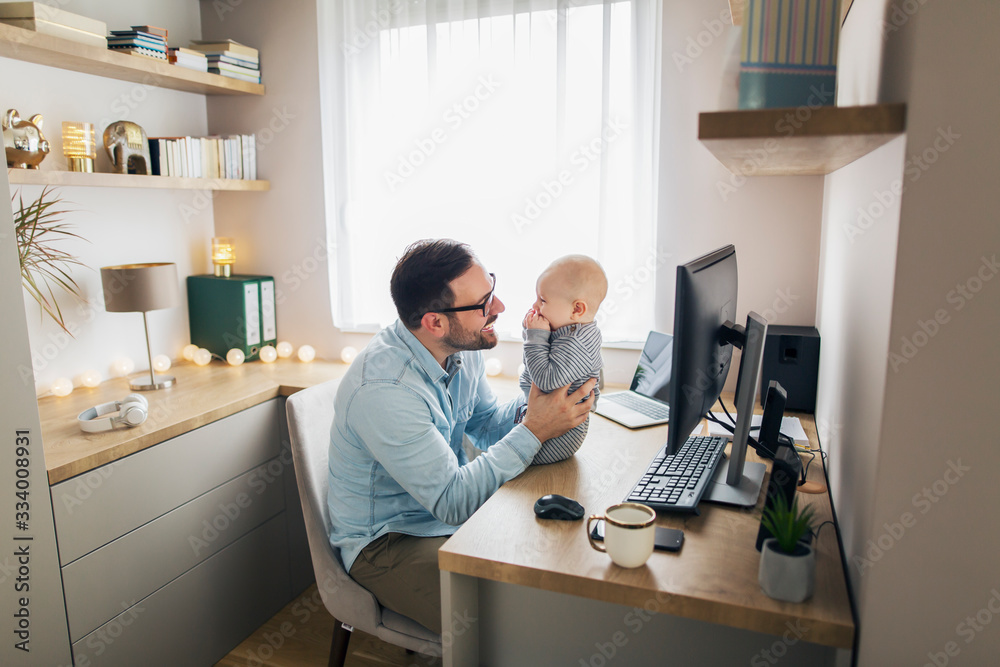 Young father working from home and babysitting his baby boy.