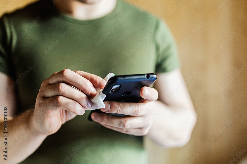 Disinfection the phone with an antiseptic using an antibacterial cloth. Close-up of hands holding a napkin with antiseptic, wiping the smartphone, covid-19 and coronavirus. Concept of personal hygiene Disinfection the phone with an antiseptic using an antibacterial cloth. Close-up of hands holding a napkin with antiseptic, wiping the smartphone, covid-19 and coronavirus. Concept of personal hygiene