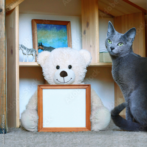 Copy spaсe, picture frame in holding hands for quarantine, kids club, center home school, stay home. Teddy bear sits near children playhouse Holds empty picture. photo