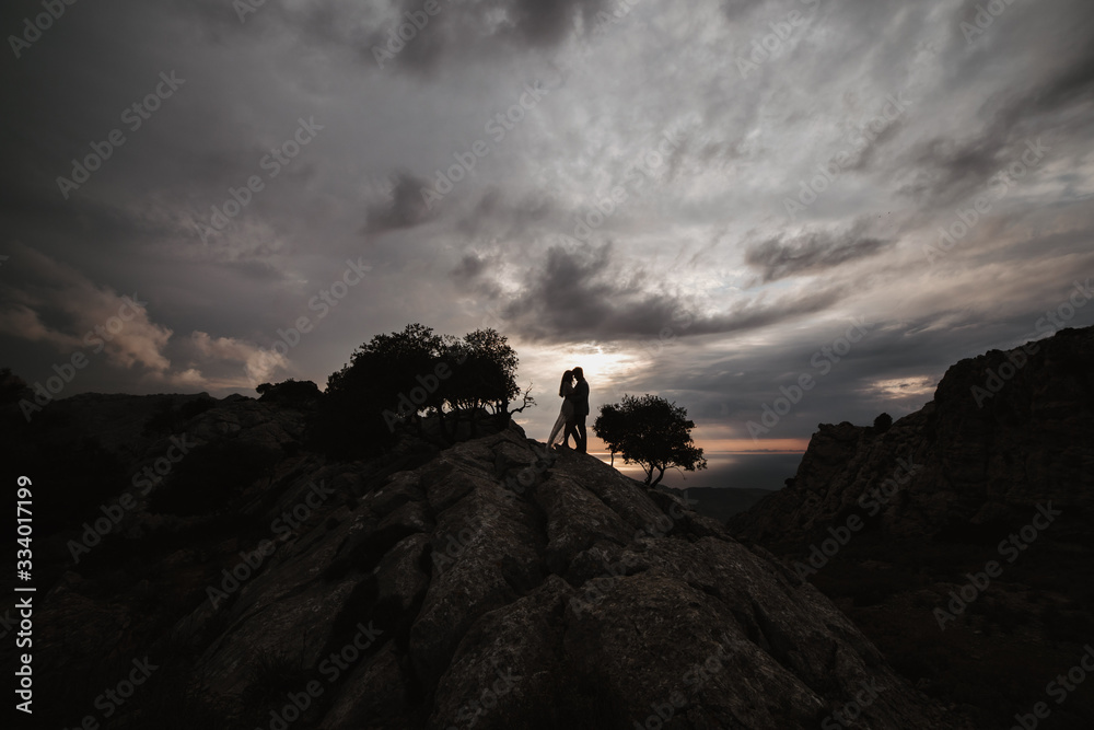 Fototapeta premium couple standing on the top of mountain, holding hands and watching sunset