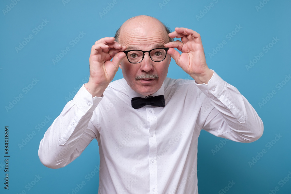 Naklejka premium Amazed senior man looking at camera through glasses having some doubts