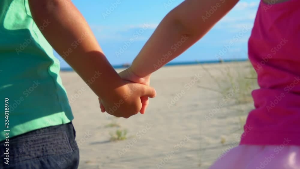 Closeup of little boy and girl in pink skirt holding hands on the beach on a sunny summer day Closeup of little boy and girl in pink skirt holding hands on the beach on a sunny summer day