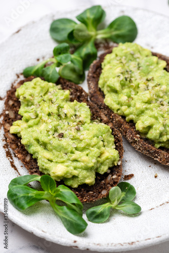 Rye bread with mashed avocado and hemp seeds. Healthy vegan avocado toast on white plate