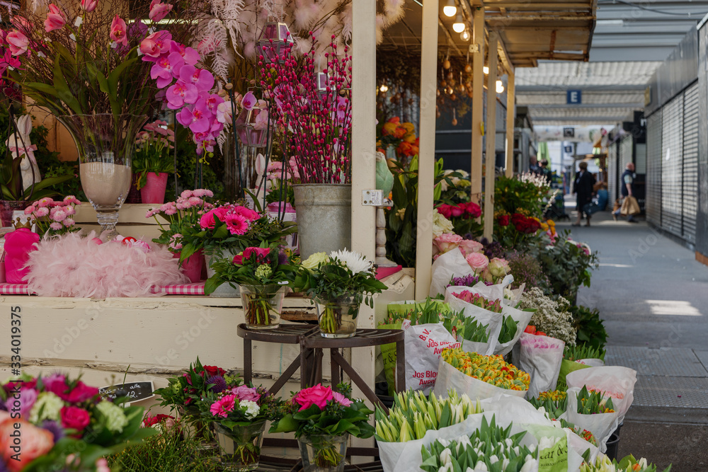 View of colourful various flowers in plastic box are sold at corridor in front of flower stall or floral shop is located in outdoor market in Europe. Typical atmosphere of flower store.   