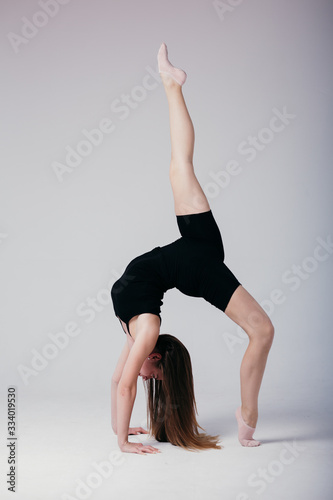 Beautiful gymnast in black sportswear standing on his hands on white background. Sporty girl doing a handstand