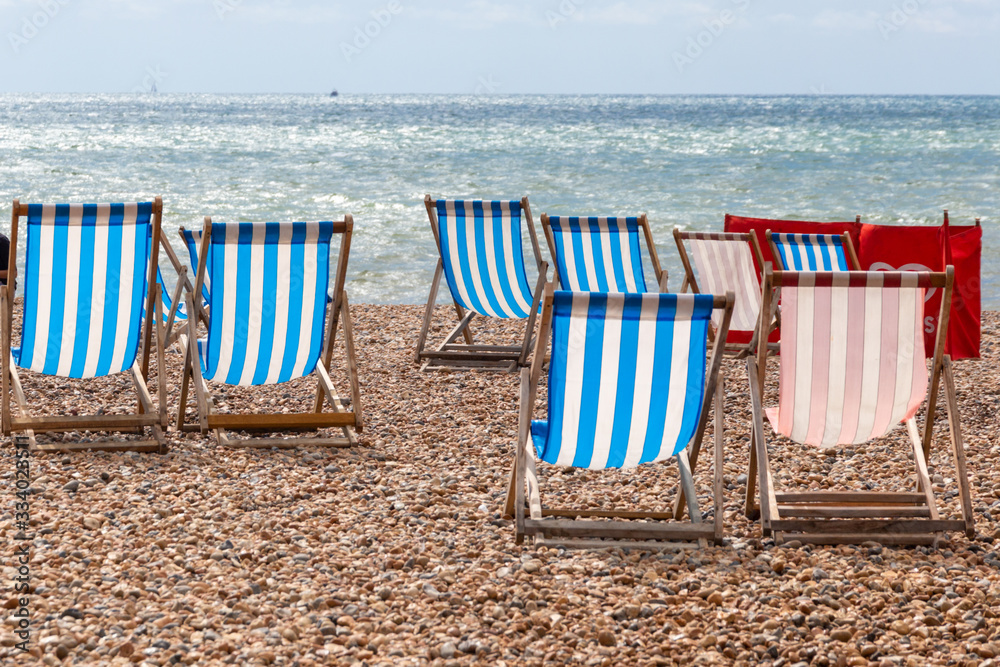 Colourful striped deck chairs for rent on the pebble beach at Brighton, East Sussex, England