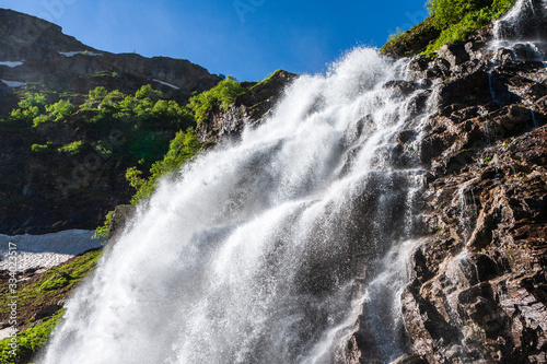 Beautiful scenic landscape of Imeretinskiy waterfall in Caucasus mountains  Karachai-Cherkess Republic. Imeretinka river waterfall at summer in sunlight with splashes and blue sky.