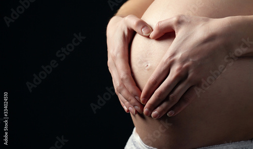Wallpaper Mural Pregnant Woman holding hands in a heart shape on her belly on black background Torontodigital.ca