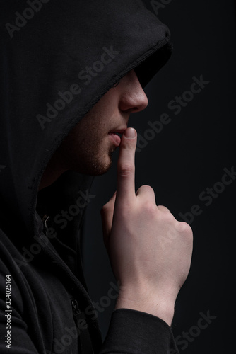 A man in a black hood on a black background, studio photography. The idea of mysticism, mystery, crime and deception