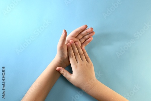 Two children's palms on top of each other on a light blue background. © uly.u.v 