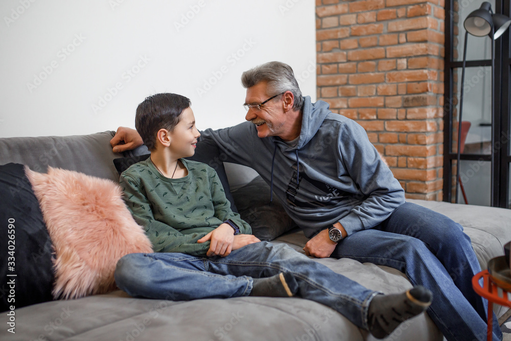 Happy grandfather sit on sofa and enjoy spending time with preschooler grandson at home