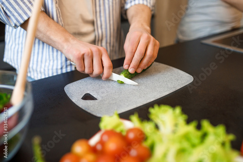 Close up photo, man cutting cucumber on cutting board, cooking time
